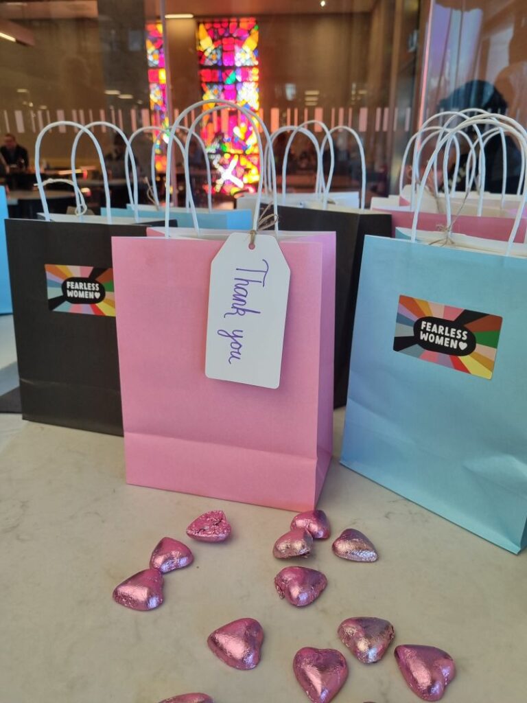 Image of paper bags with "thank you" written on them. They sit on a table with pink foil-wrapped chocolate hearts in front of the bags